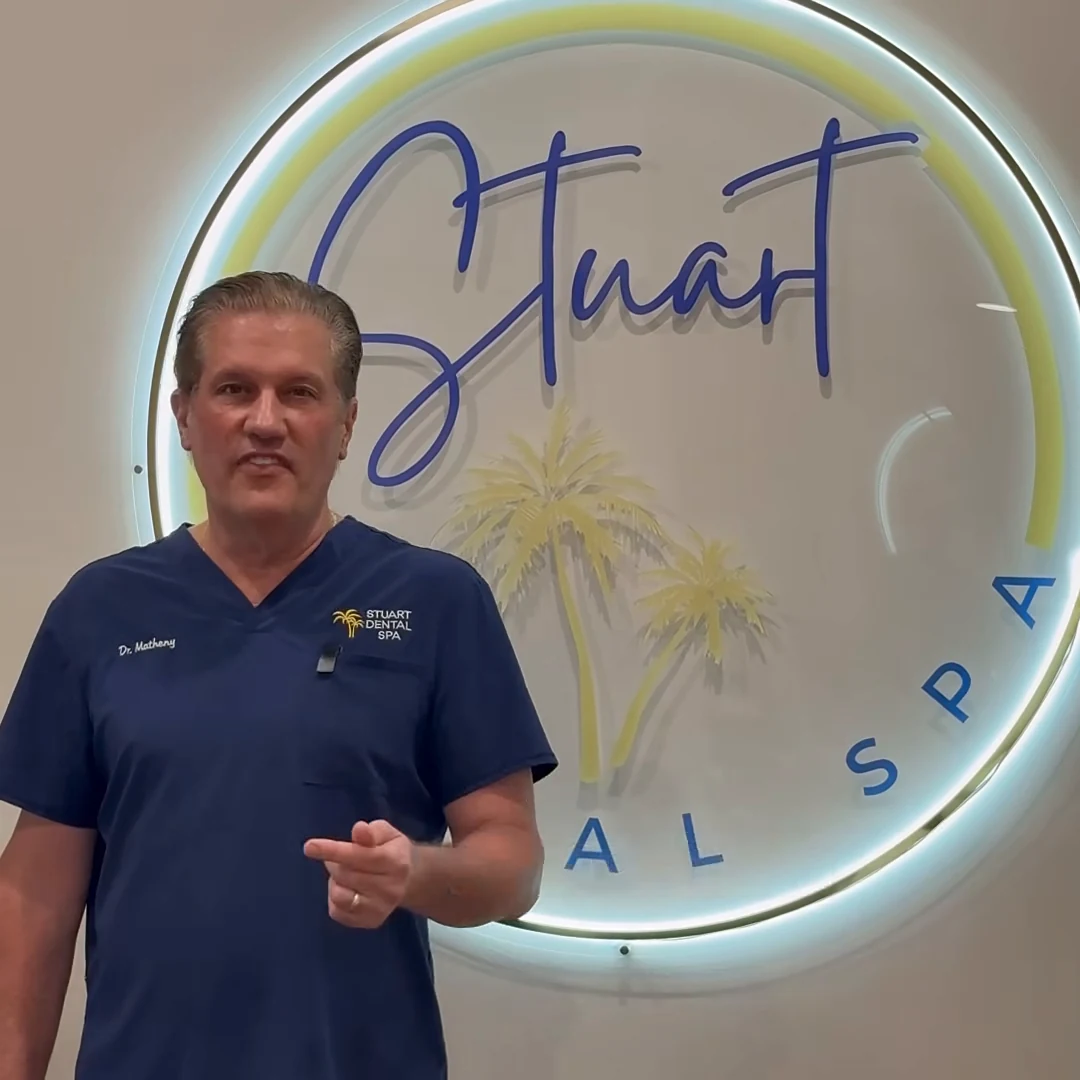 Frame from a Stuart Dental Spa video ad, showing Dr. Matheny in navy scrubs in front of the illuminated practice logo