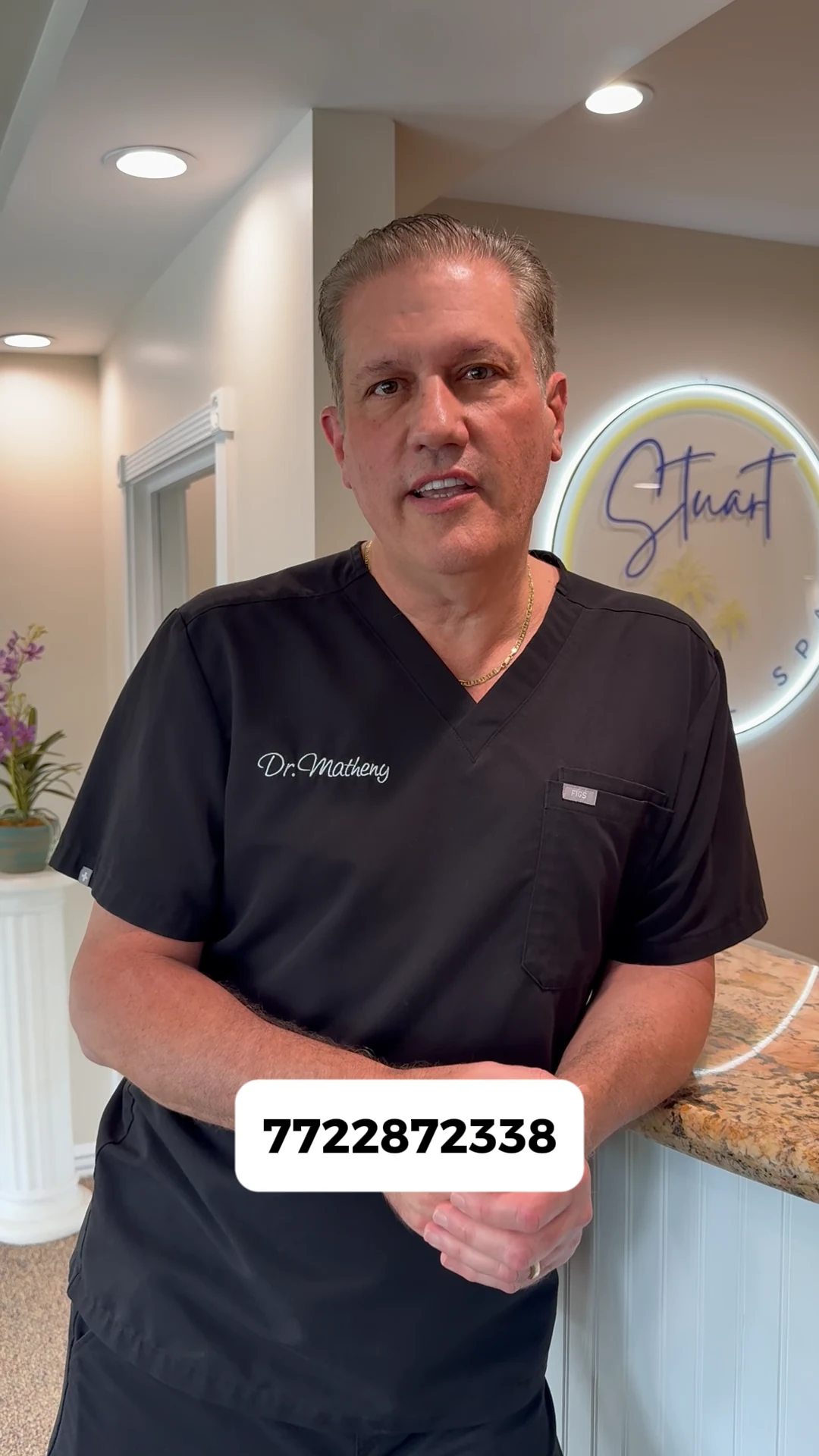 Frame from a Stuart Dental Spa video ad, showing Dr. Matheny at reception in black scrubs with the practice phone number in the original caption